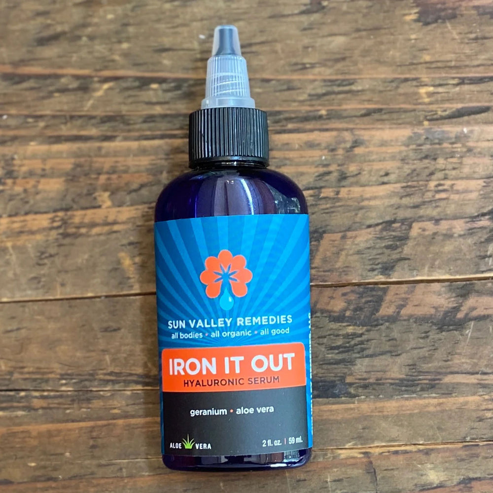Two ounce cobalt bottle of Iron It Out, a Hyaluronic Serum. The blue label indicates it is made with aloe vera and geranium