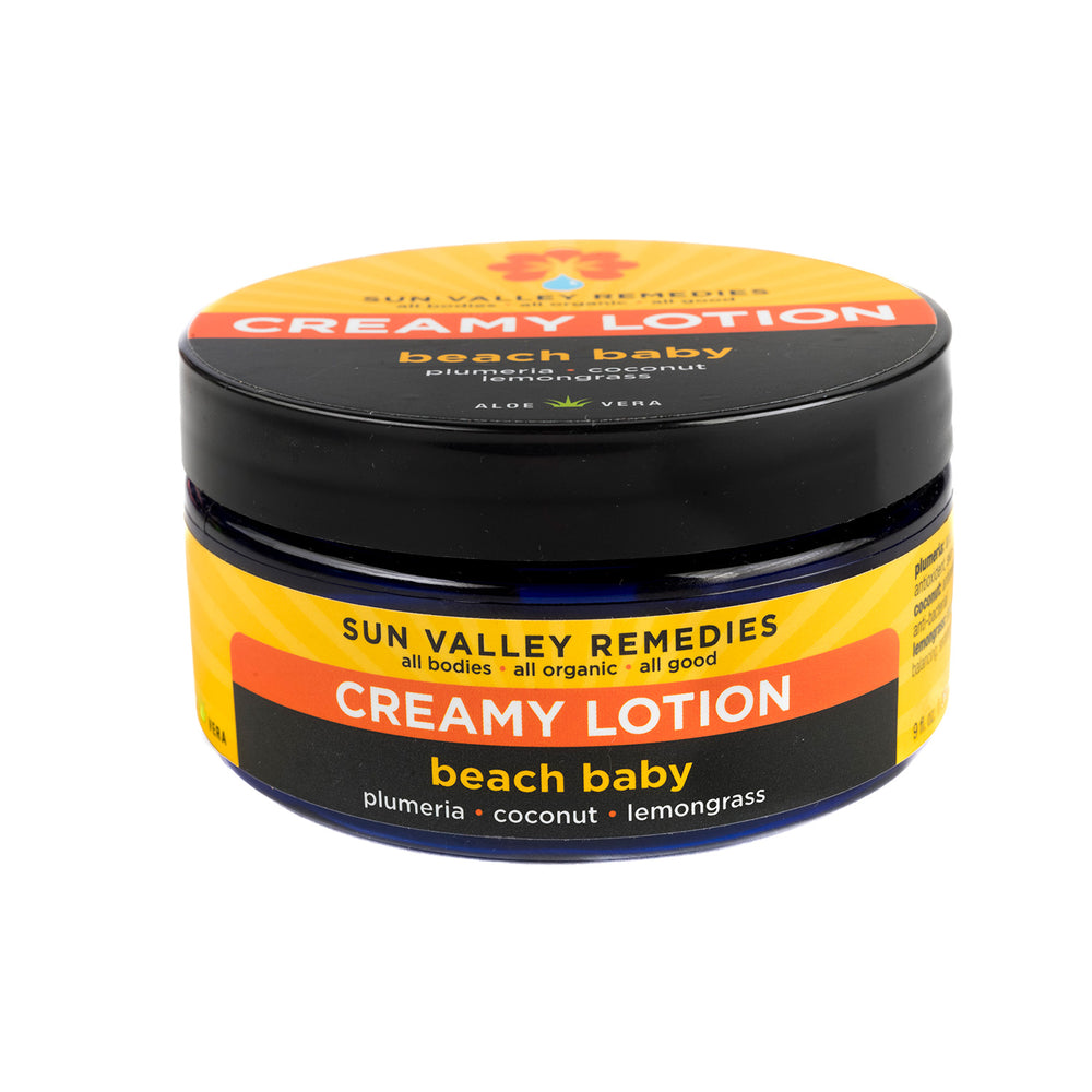 Nine ounce cobalt jar of Beach Baby Creamy Lotion.  The label indicates the aromatherapy is plumeria, coconut, and lemongrass