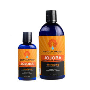 Two cobalt bottles of Energizing Jojoba Oil. The orange label indicates the aromatherapy is peppermint, frankincense and lemon