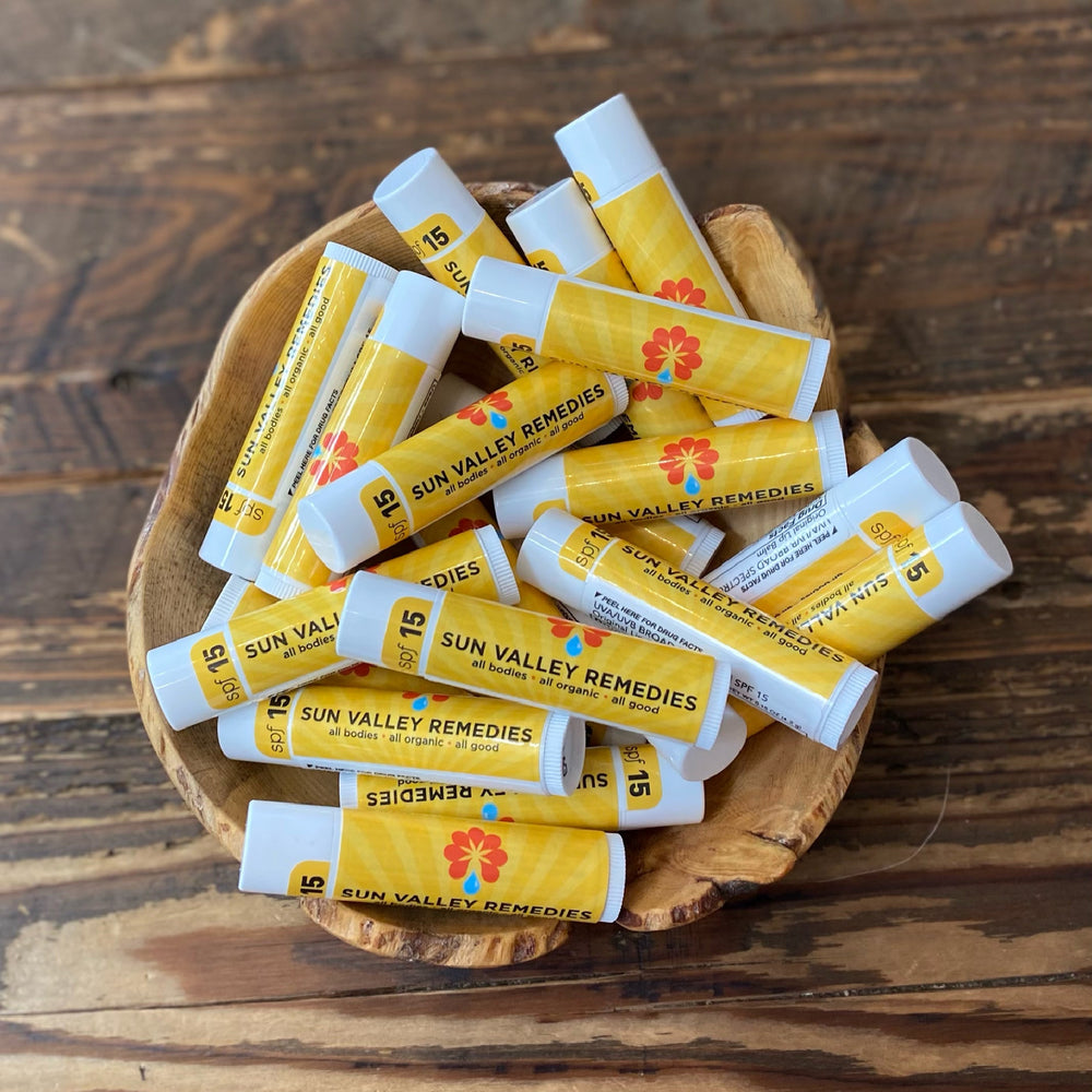 white tube of Lip Balm. Yellow label indicates it has SPF fifteen, is for all bodies is all organic and all is good