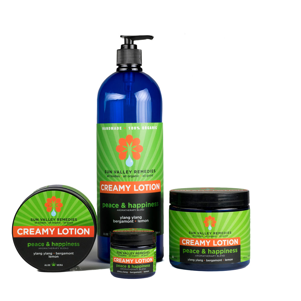 Four cobalt containers of Peace and Happiness Lotion. The green label indicates the aromatherapy is ylang ylang, bergamot, lemon