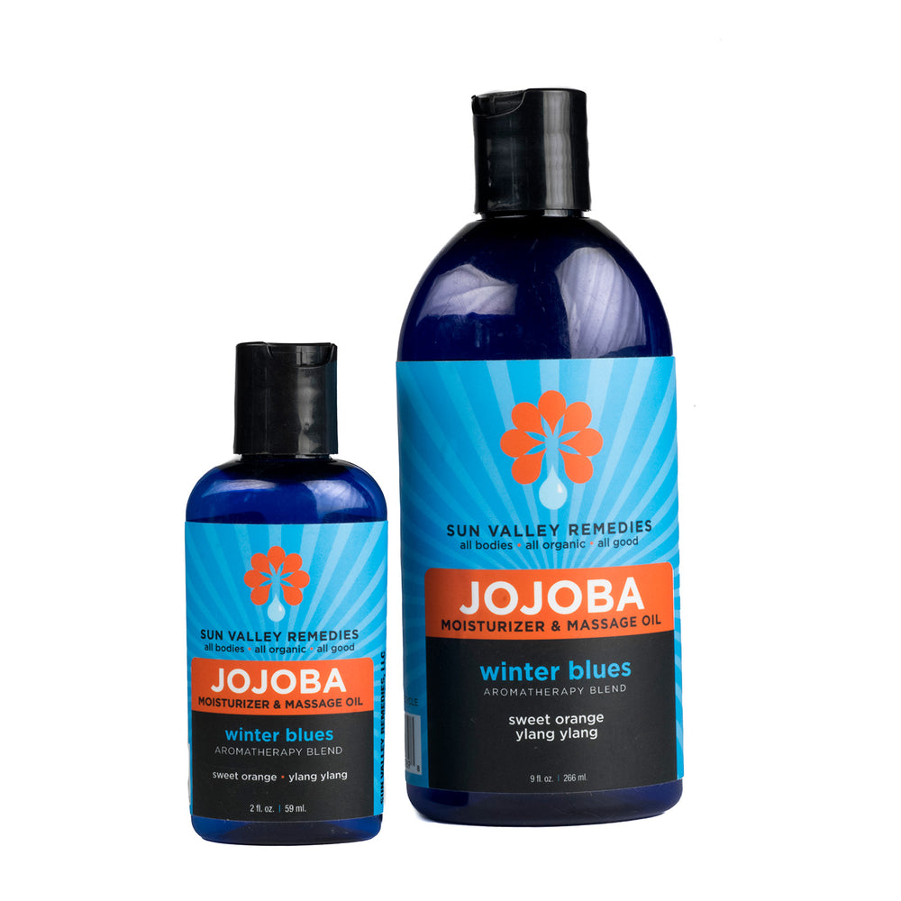 Two cobalt bottles of Winter Blues Jojoba oil. The blue label indicates the aromatherapy is sweet orange and ylang ylang.